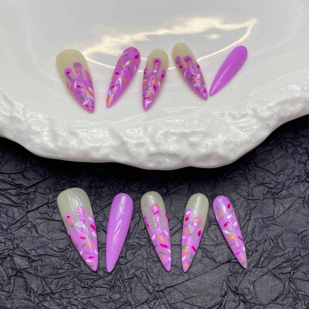 Handmade press-on nails featuring adorable hand-painted ice cream cones in shades of purple on trendy almond-shaped nails.